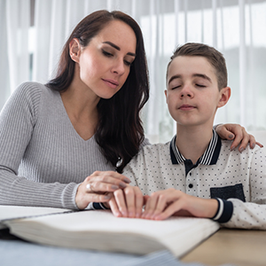 Adolescent boy with visual impairment reading braille with mentor